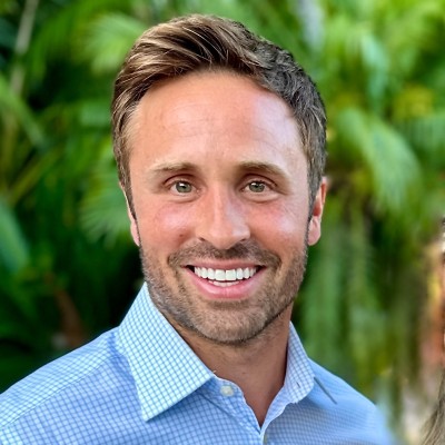 Close up of a young white male, with a short stubble brown hair, smiling and wearing a light blue collared shirt